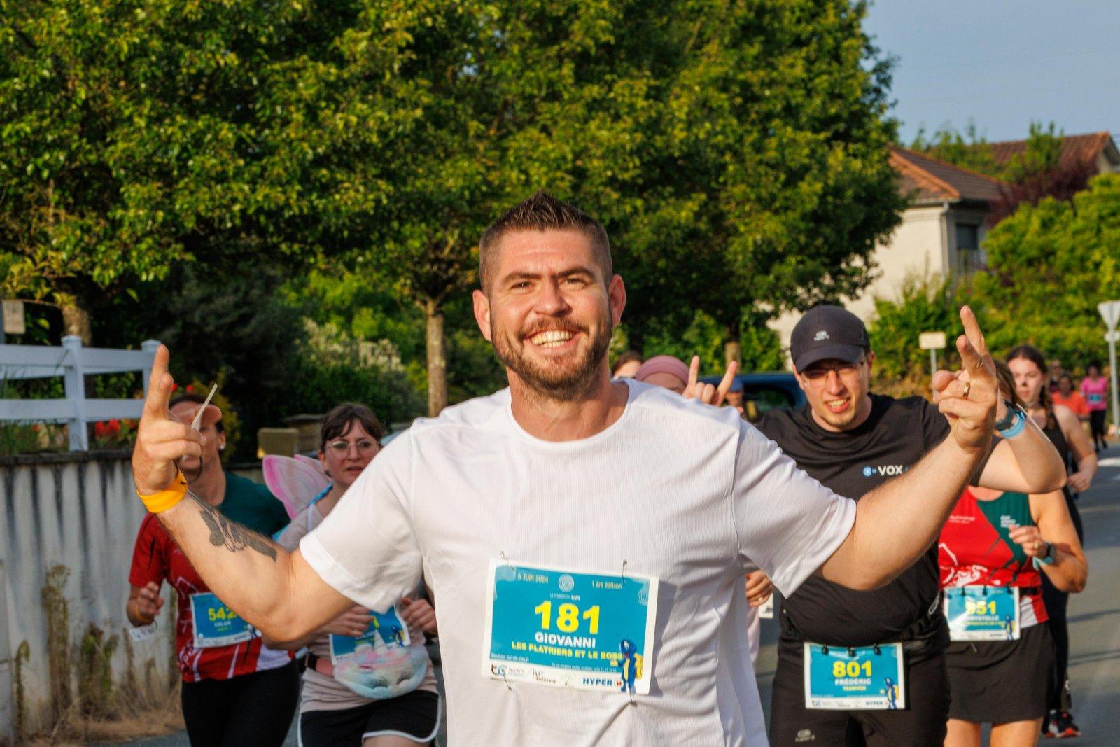Un coureur lève les bras et sourit à l'objectif, au milieu du peloton